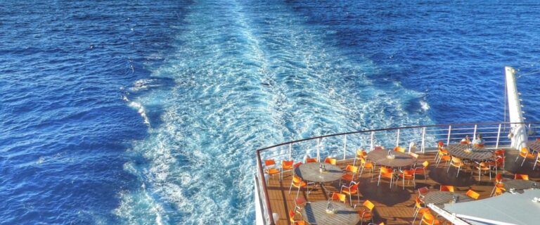 Photo of a cruise ship and the wake behind it in the sea.